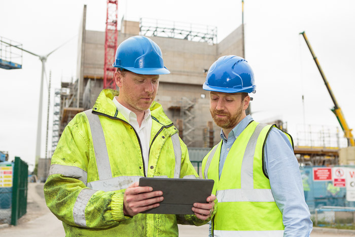 Two men in hard hats on building site looking at tablet