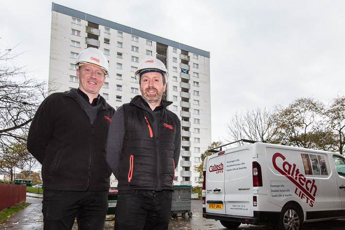 Two men in hard hats in front of tower block